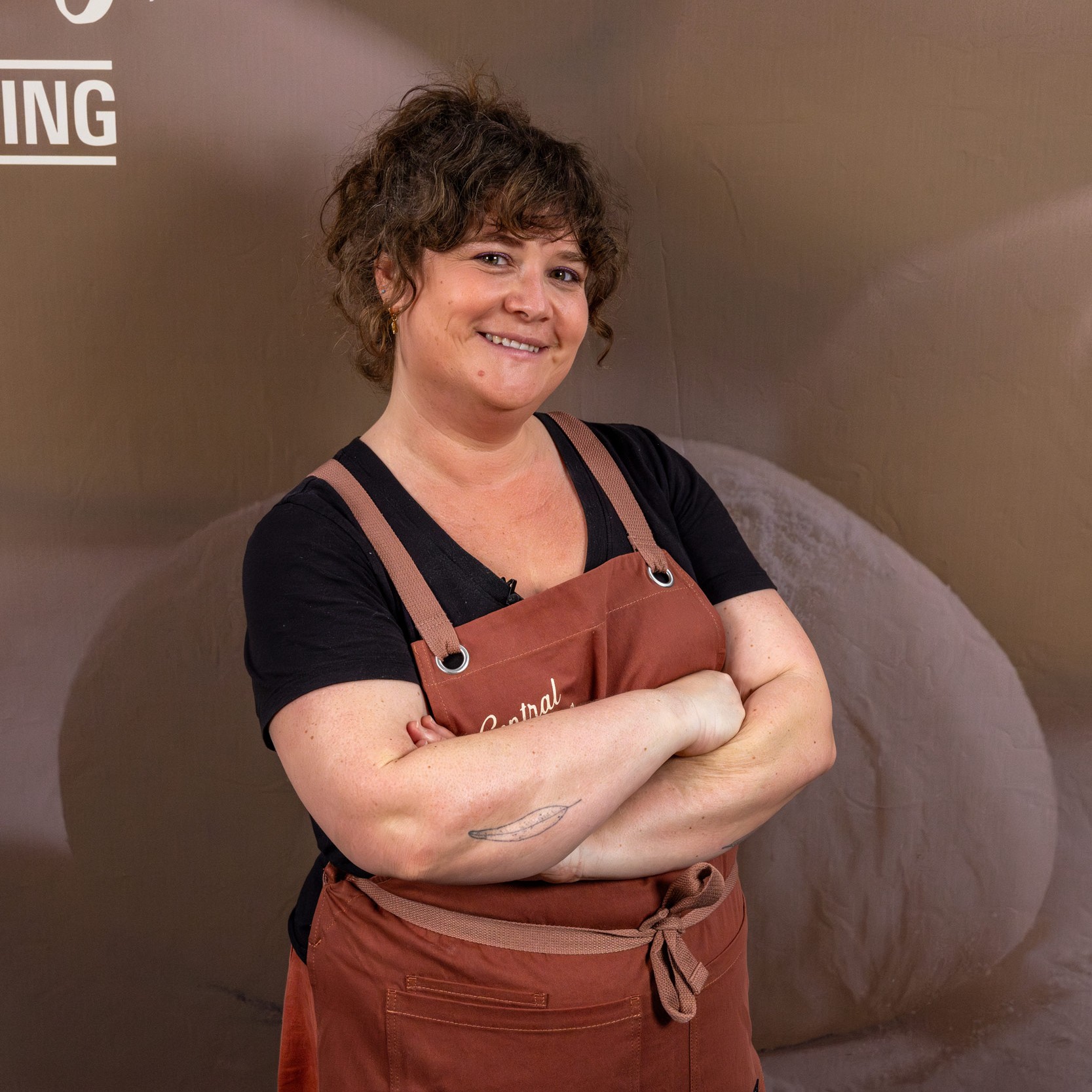 Laila smiling in a rust-colored Central Milling apron, arms crossed